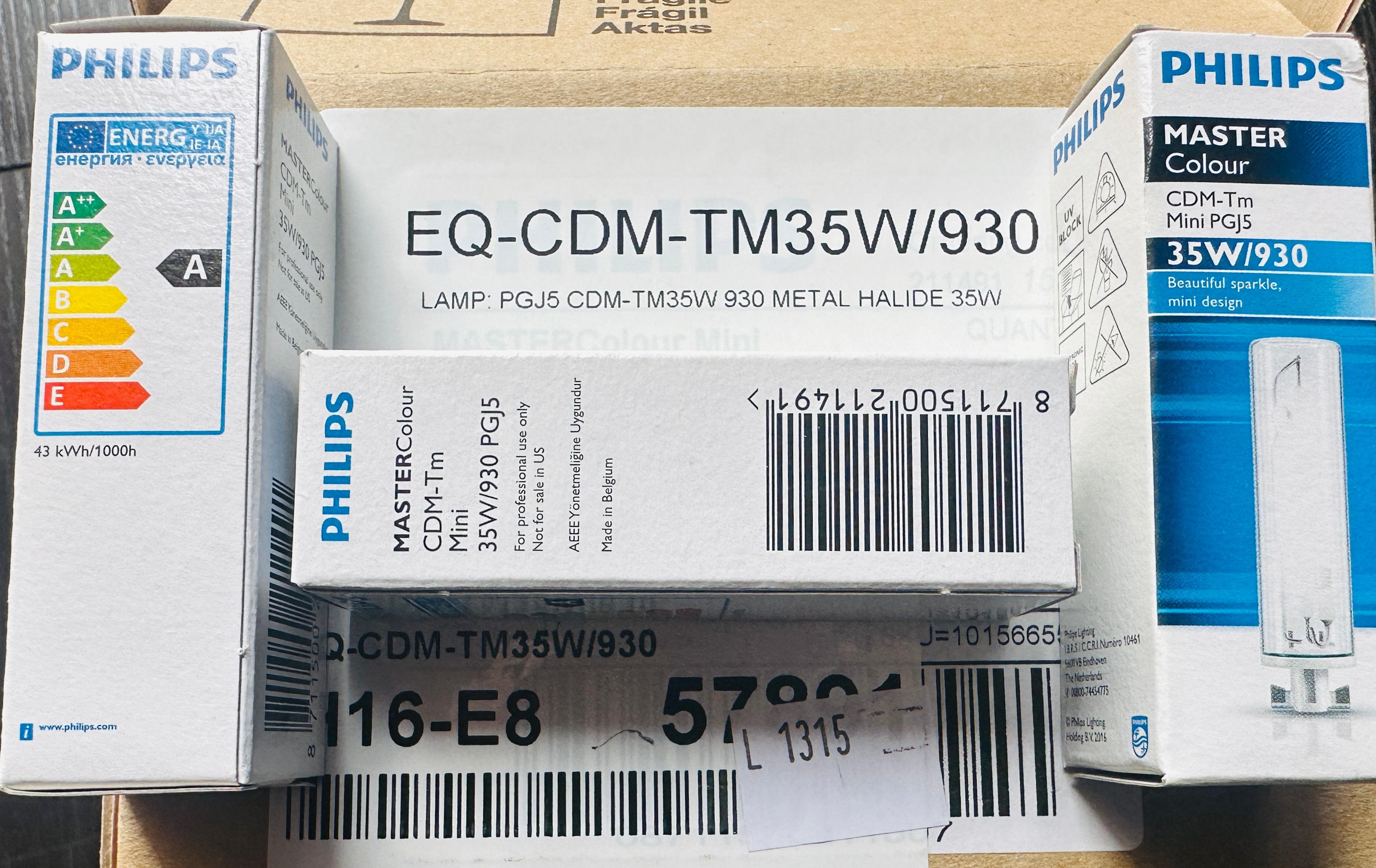 Several Philips LED light bulb packaging boxes stacked together on a cardboard surface. The front box reads EQ-CDM-TM35W/930 and shows Philips branding,能效 labels, and barcodes.
